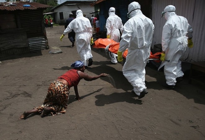 Một người phụ nữ ném nắm đất về phía thi thể của em gái bị nhiễm ebola khi nhân viên y tế đem bệnh nhân đi hỏa táng tại Monrovia, Liberia, ngày 10/10. 