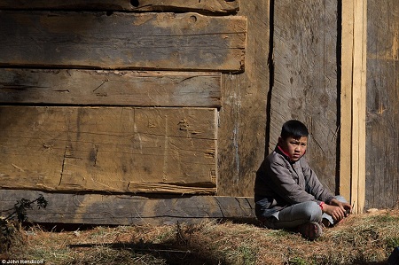 Một&#10;cậu bé người Bhutan ngồi một mình trước cửa nhà.